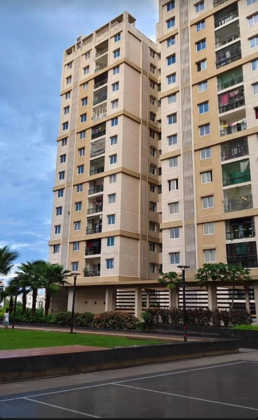 A cream and beige apartment tower with stacked balconies and a landscaped podium, photographed from across the road