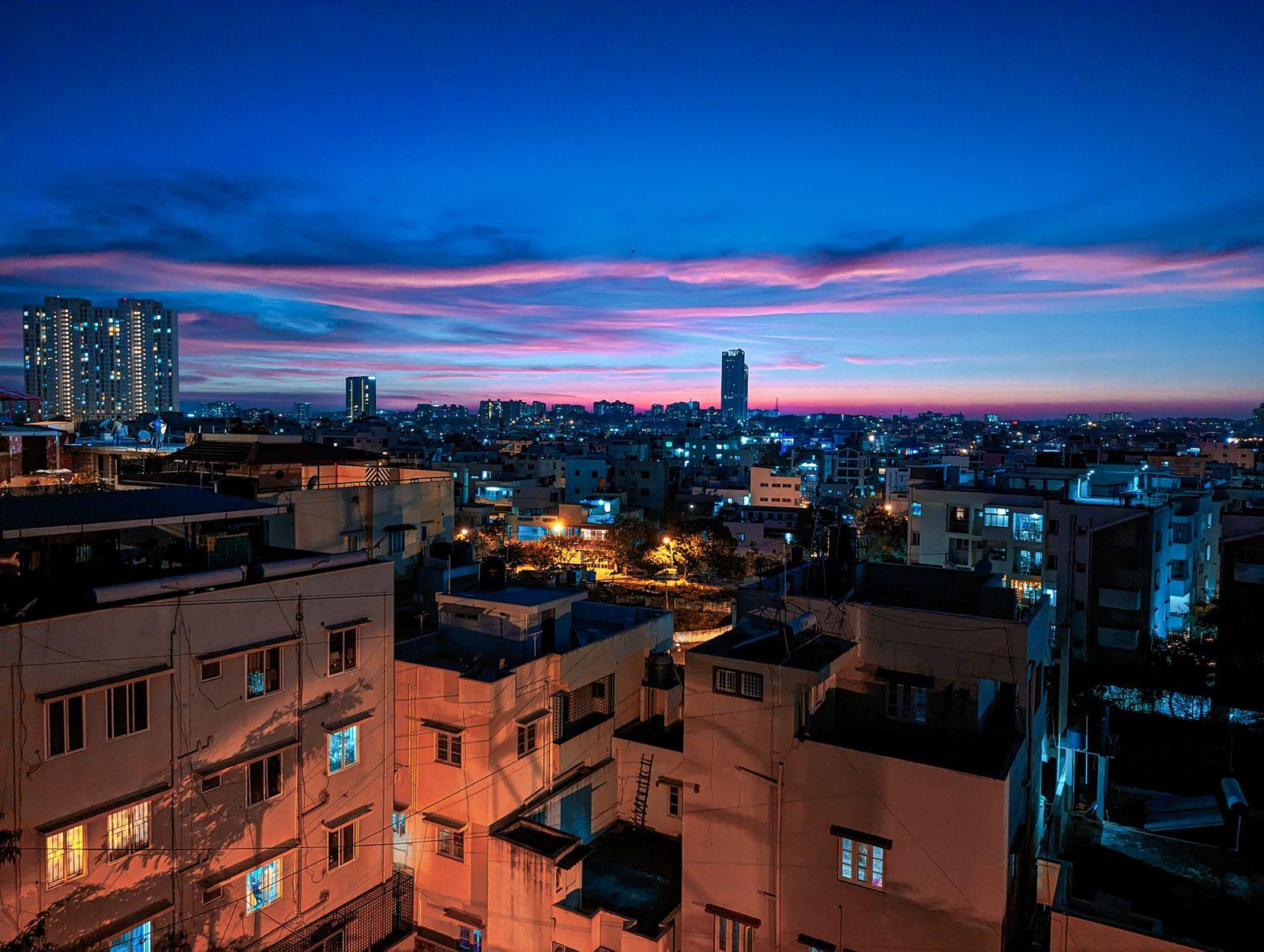 Bengaluru at dusk: low-rise rooftops and scattered high-rise towers beneath a pink and deep blue sunset sky