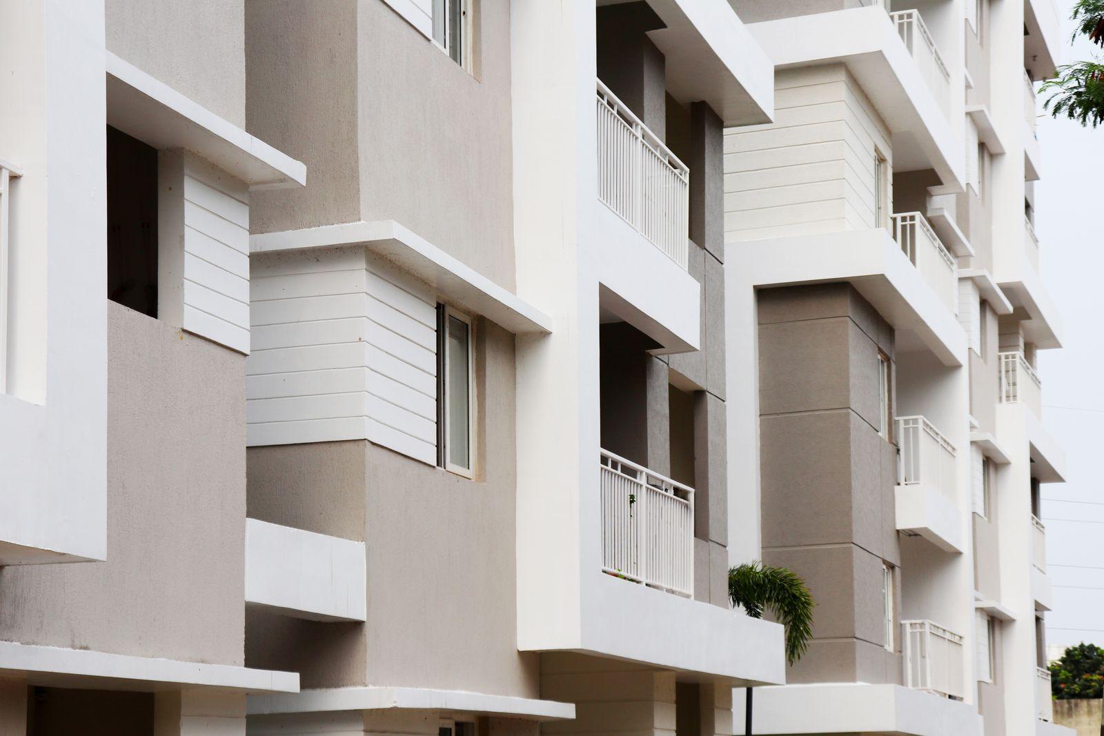 A modern apartment block seen from below, with clean white balcony slabs, pale grey columns and metal railings on an even painted finish